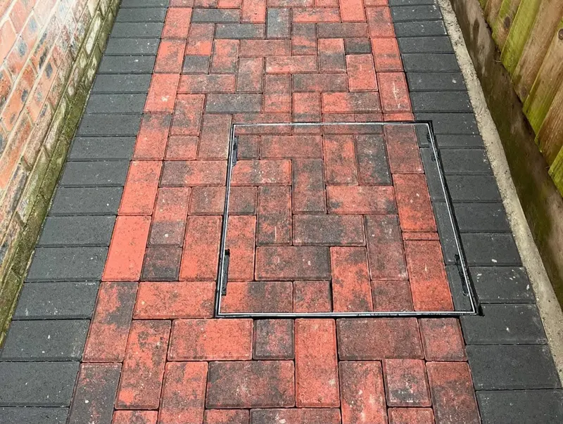 Semi-circular brick raised bed topped with brindle herringbone block paving and charcoal borders on a matching lower patio.