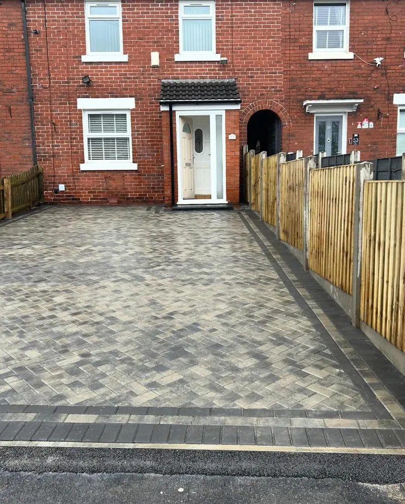 Warm brindle block paving with a charcoal border across the front garden and continuing down the side of a brick semi.
