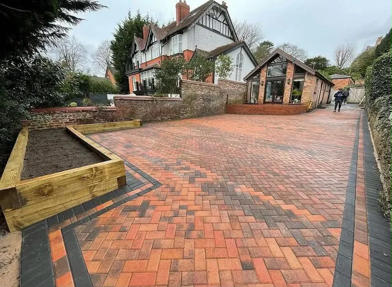 Blended grey herringbone block driveway with a dark double border replacing the front garden of a red brick terraced house.