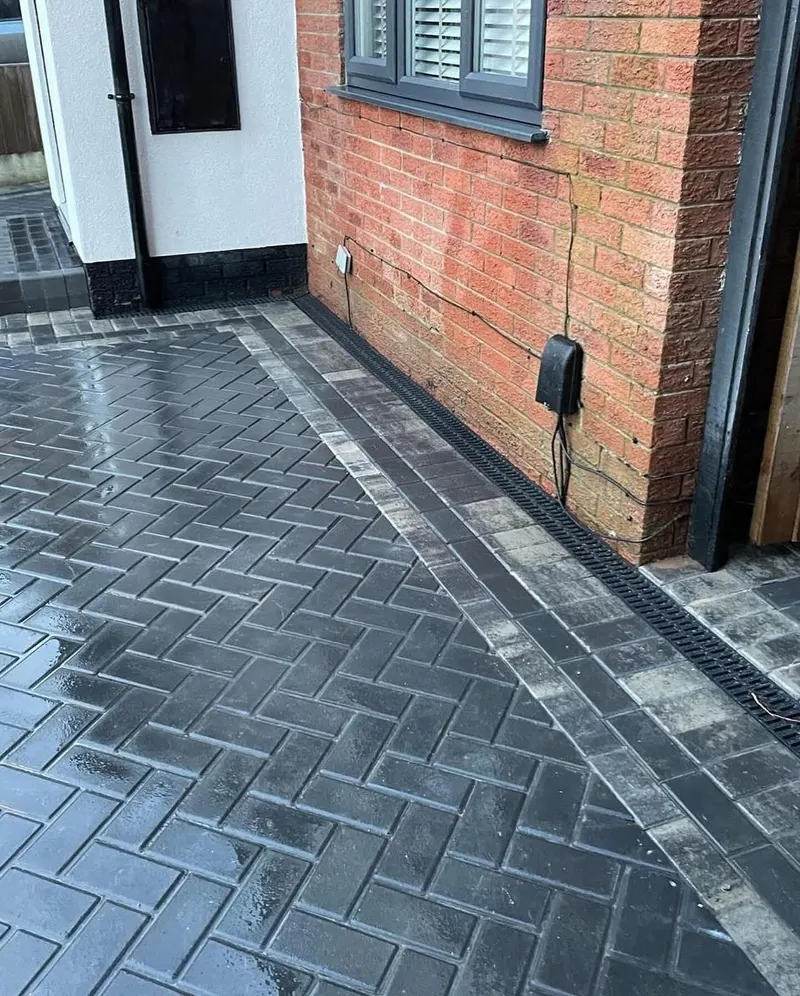 Charcoal herringbone block driveway with silver double borders, ornate lamp post and slot drain along red brick.