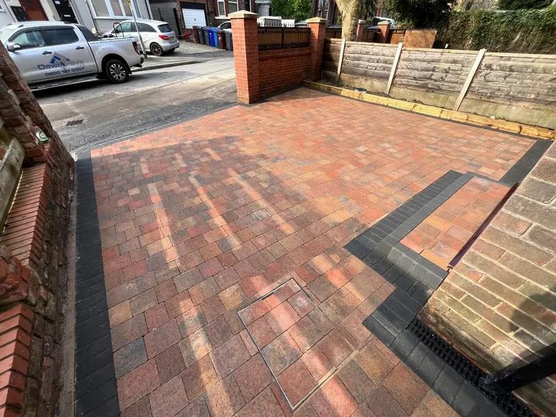 Close detail of charcoal herringbone block paving, light and dark border courses and a linear drain at the base of brickwork.