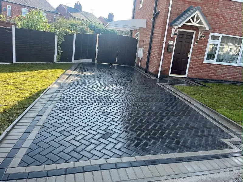 Multi-toned brindle block paving with charcoal edges, bullnose step, slot drain and paved manhole wrapping a front door and side path.