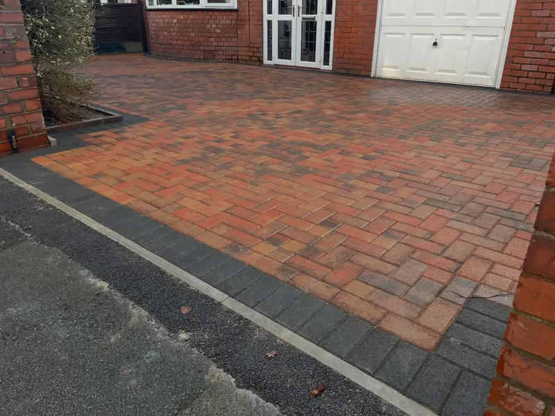 Charcoal herringbone block driveway with grey and dark borders, lawn panels and a path leading to dark wooden gates.