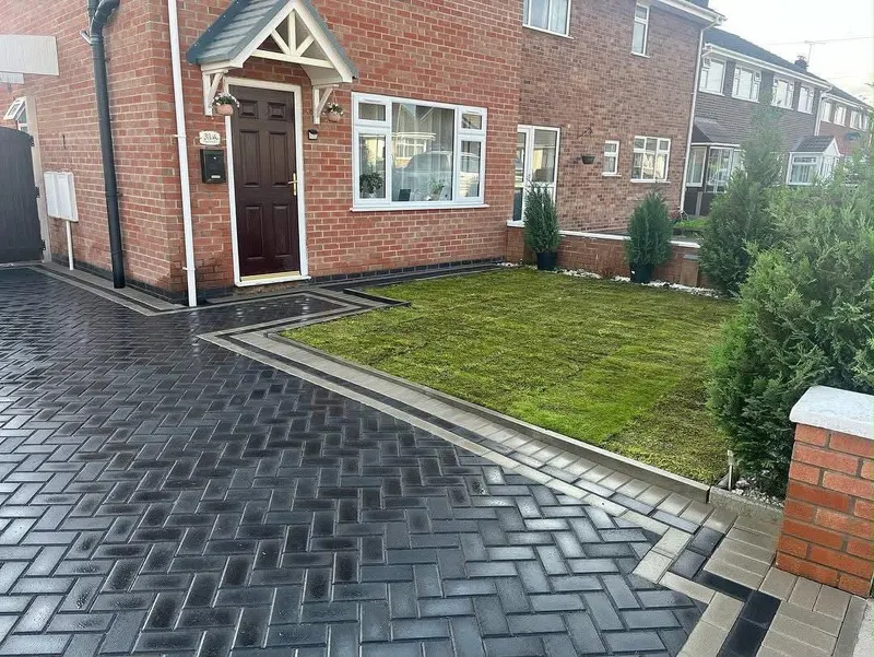 Charcoal herringbone block side driveway with light grey outer border, lawn on one side and tall wooden gates ahead.
