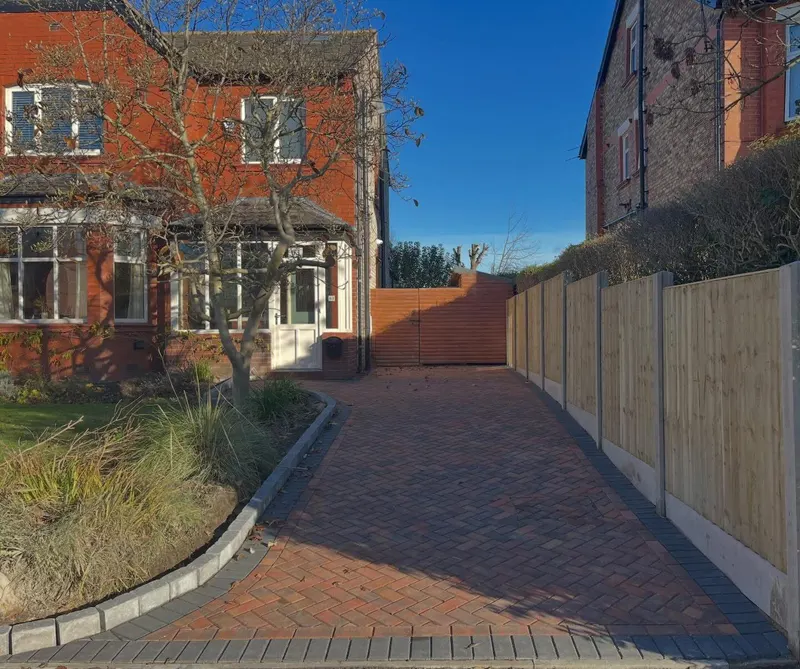 Brindle herringbone block driveway with charcoal soldier edging leading to a white garage and arched glass doors on red brick.