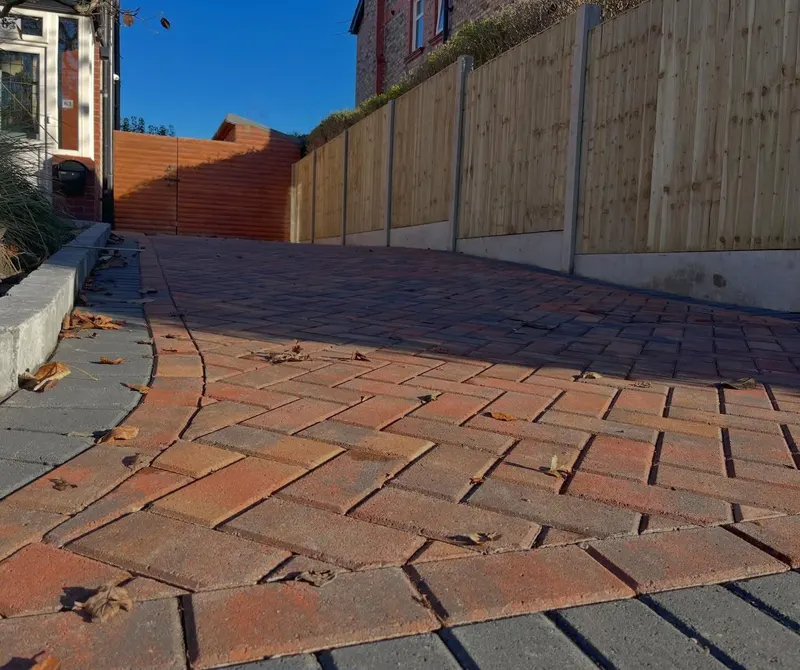 Extended brindle herringbone block driveway with charcoal border, granite kerb edging and timber fence along a brick property.