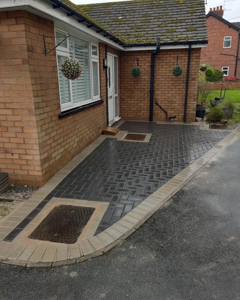 Fresh brindle herringbone block paving with dark soldier border and raised kerb separating planting from a wooden fence line.