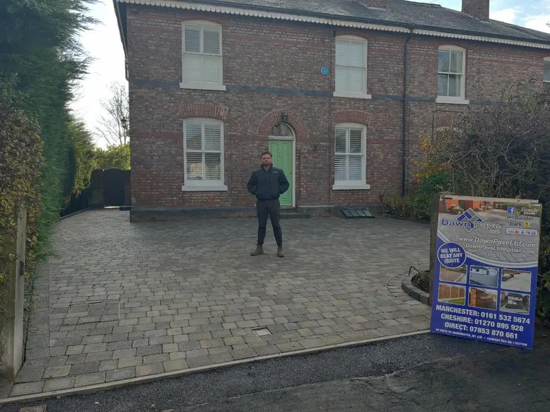 Red and charcoal brindle herringbone block driveway with dark border in front of a brick house on a bright winter day.
