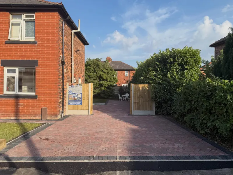 Mixed grey and brown tumbled block paving across the front of a red brick terrace, with hedge boundary and company signage.