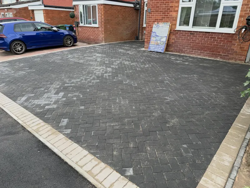 Detail of charcoal herringbone block paving framed by triple buff and dark borders sweeping in a semicircle beside a slot drain.