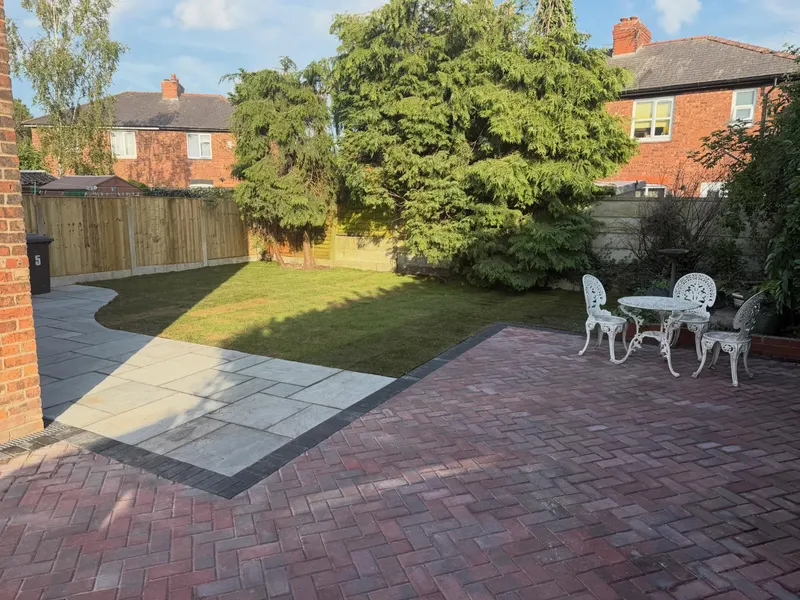 Elevated view of charcoal herringbone block paving with light border, EV charger on the wall and street parking beyond.