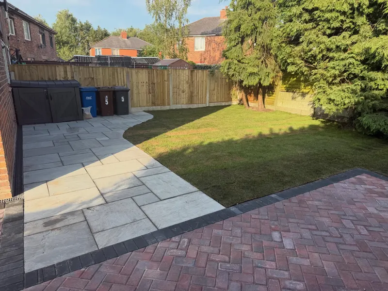 Back garden combining red brindle herringbone block patio with charcoal edging and curved grey stone slabs around a lawn.