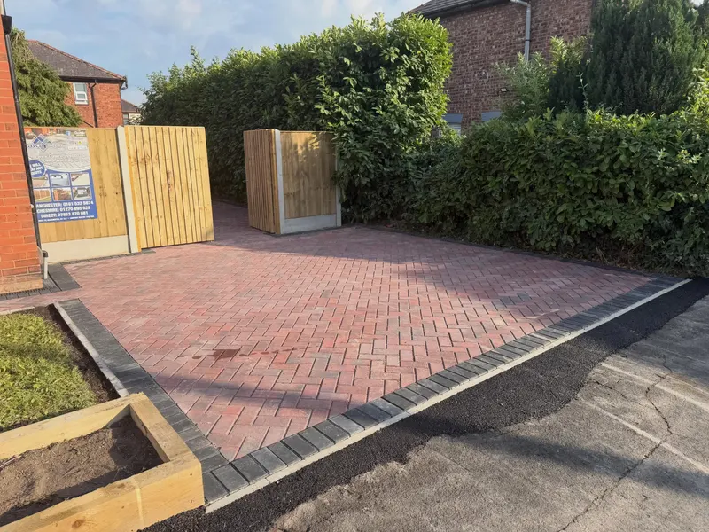 Rear garden with grey stone slab path, central lawn and a red herringbone block patio corner bordered in charcoal blocks.