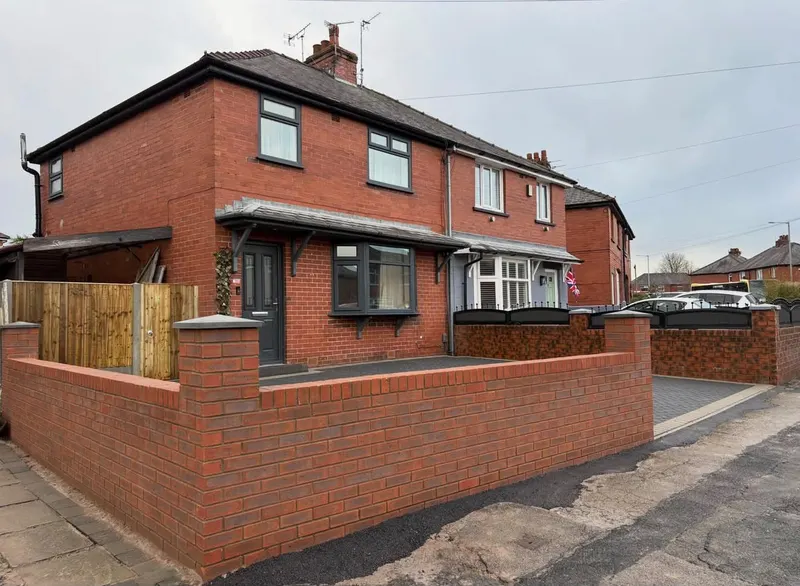 New low red brick front wall with square piers and dark grey flat copings, enclosing a black tarmac driveway in front of a semi-detached brick house.