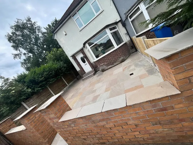 Red brick garden walls and pillars with light stone copings bordering a multi-tonal natural stone patio at a white and brick frontage.