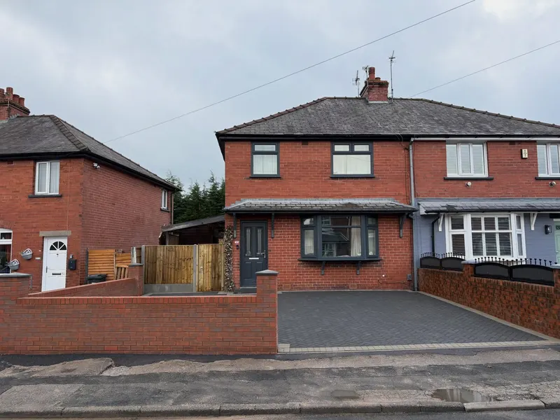 Freshly built red brick front wall with a pier cap beside a dark herringbone block-paved drive at a grey-doored semi-detached house.