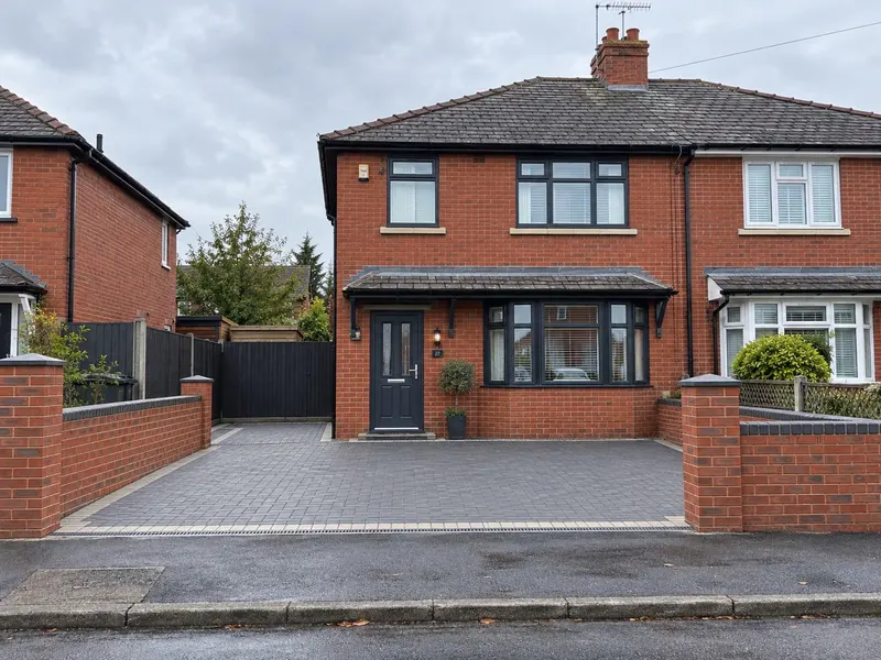 Matching red brick entrance walls with dark grey coping stones lining a charcoal block-paved driveway at a modernised semi-detached home.