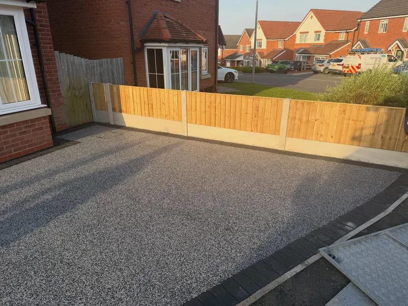 Fresh vertical timber fence panels on concrete posts and gravel boards, running beside a speckled grey resin-bound driveway with a dark block-paver border.