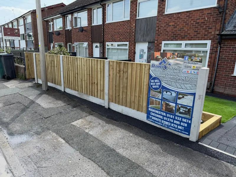 Continuous wooden closeboard fencing with concrete posts and gravel boards along a terraced front garden, with artificial grass visible behind the panels.