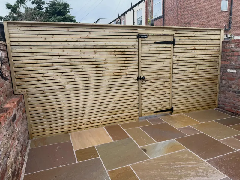 Modern horizontal timber slat fence and matching gate with black metal hardware, fitted between red brick boundary walls above a multi-tonal stone patio.