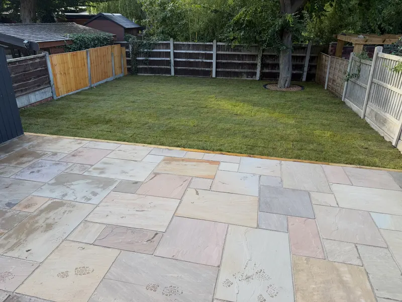 Multi-coloured natural stone flags separated from a rectangular lawn by a timber sleeper edge, enclosed by mixed wooden fencing.