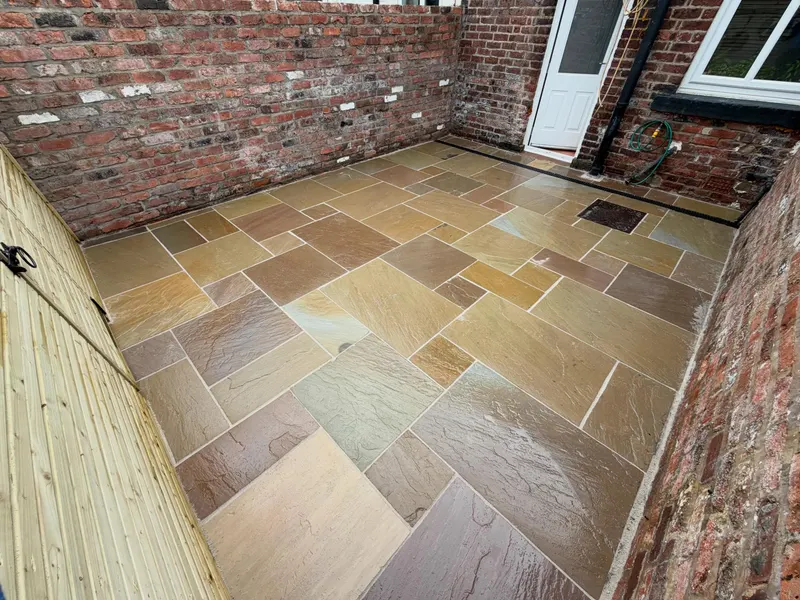 Multi-toned riven stone slabs in a tight courtyard enclosed by aged brick walls and a vertical timber fence, with a white door and channel drain.