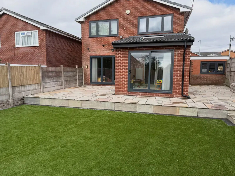 Multi-tonal natural stone paving on a raised platform along a brick extension, with stone-clad edges facing a bright green lawn.