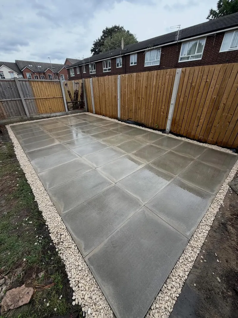 Smooth light grey square slabs in a neat grid, ringed by cream decorative gravel and new timber fencing in a suburban back garden.