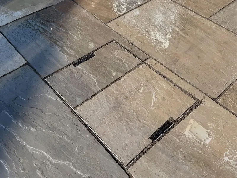Top-down view of a recessed metal manhole frame infilled with matching multi-toned riven stone slabs and dark pointed joints.