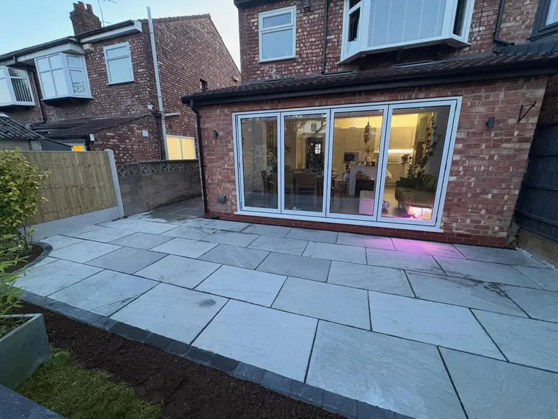 Large light grey rectangular slabs in stretcher bond with a charcoal block border, outside bi-fold glass doors on a brick extension.