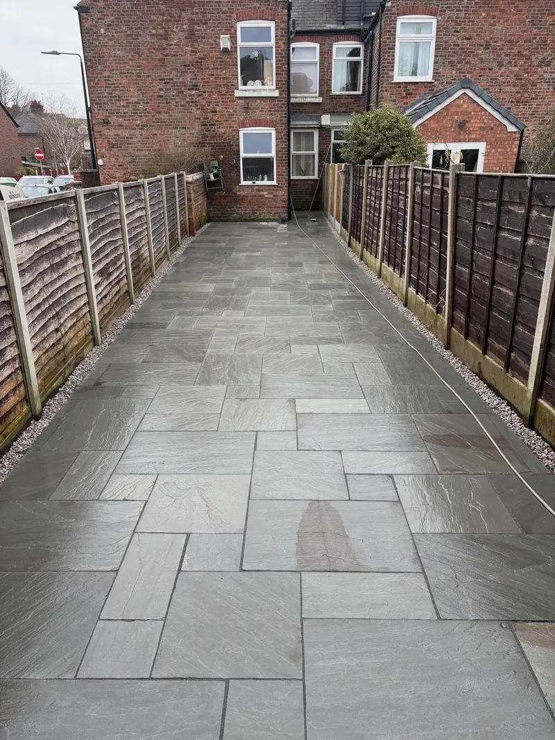 Grey riven stone slabs in mixed sizes down a narrow garden strip, with gravel borders and wooden panel fencing on both sides.
