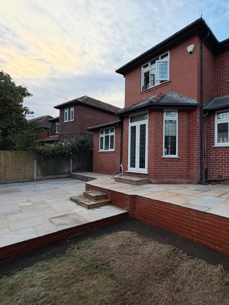 Variegated natural stone patio on upper and lower tiers linked by wide steps, supported by red brick walls matching the house.