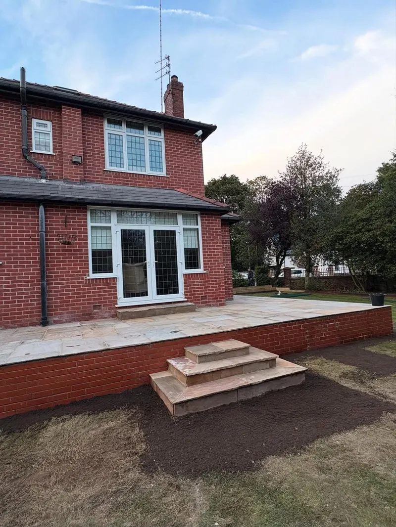 Multi-tonal natural stone flags on a raised patio with matching brick retaining walls and wide steps up to white French doors on a red brick house.