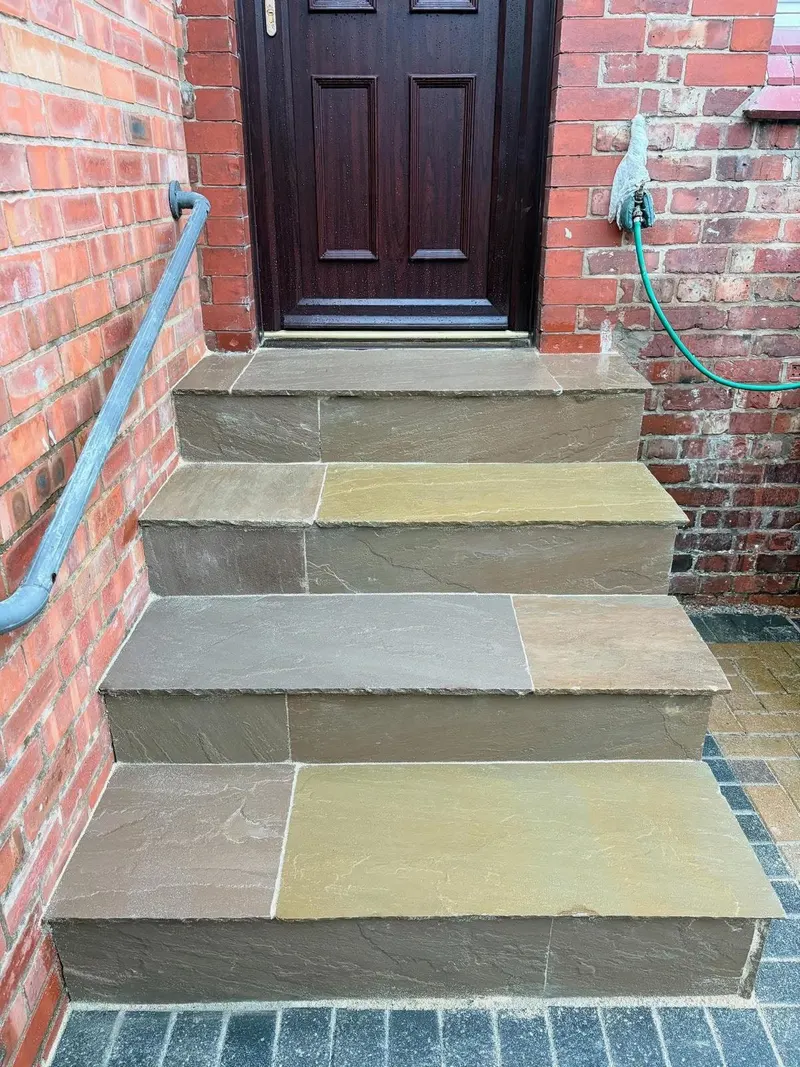 Four broad steps built from multi-coloured riven stone slabs between brick walls, meeting a dark block-paved area at the base.