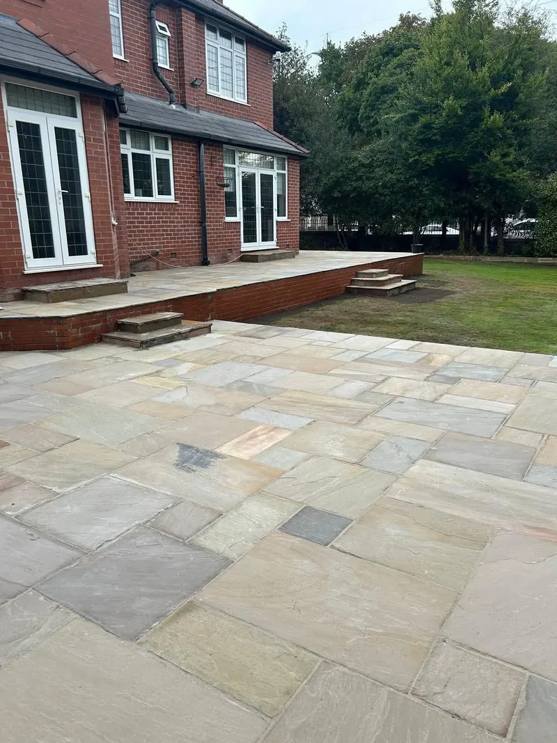 Two-tier natural stone patio with brick terrace wall, shallow steps and a lower paved area opening onto grass at a red brick property.