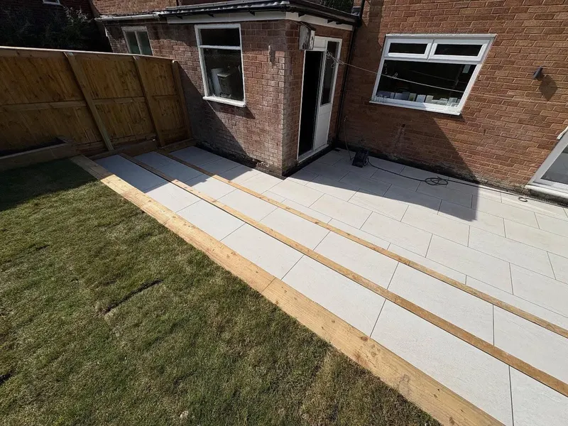 Three stepped tiers of large pale grey slabs separated by timber sleepers, running from patio doors down toward the garden lawn.