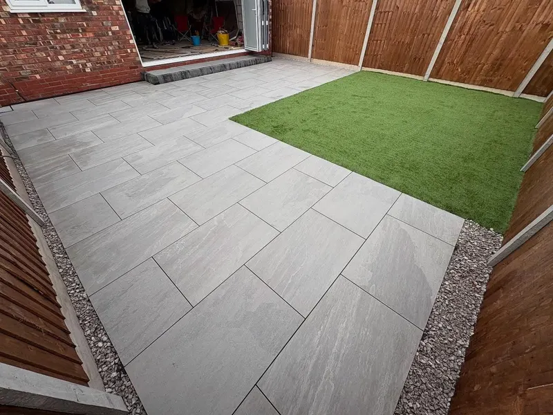 Contemporary backyard combining large grey stone slabs, a rectangular patch of artificial turf and gravel strips along a wooden fence.
