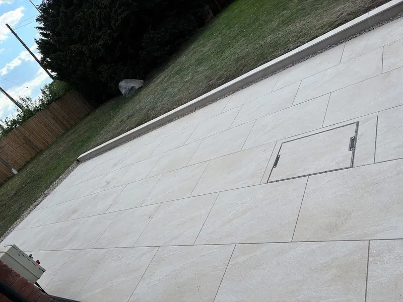 Light-toned large slabs in offset rows with a recessed manhole cover infilled to match the stone, edging onto a green lawn.