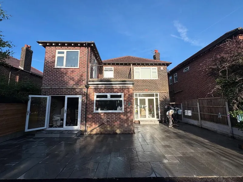 Expansive dark grey rectangular paving across the back of a red brick house, with a small matching step to open French doors.