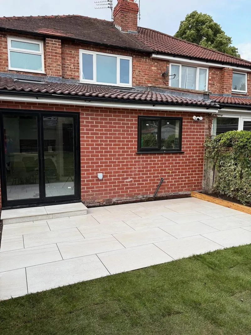 Large light grey rectangular pavers in running bond outside a new red brick single-storey extension with black-framed glass doors.