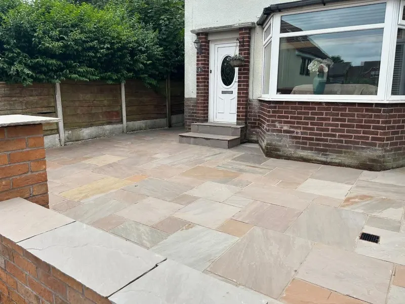 Multi-tonal riven slabs with two steps to a white front door, low brick wall topped with stone copings and integrated drainage grate.