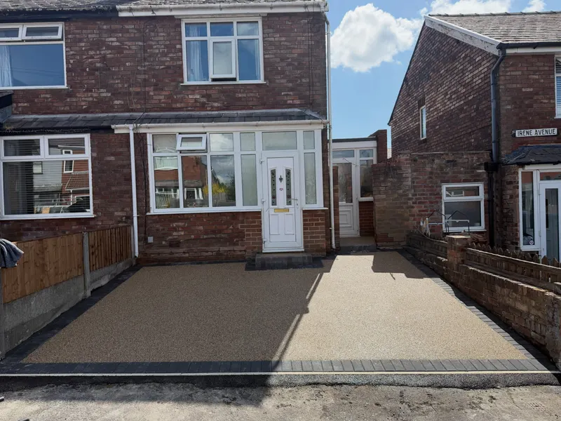 Light tan resin bound driveway framed by a dark block paving border in front of a red brick semi-detached house.