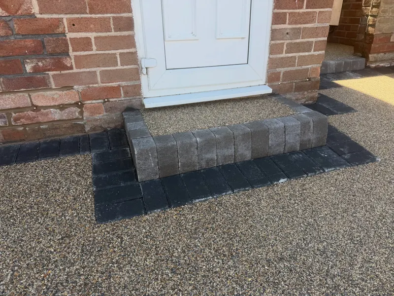 Front door step finished with buff resin on the tread and charcoal block pavers on the riser and side borders against red brick walls.