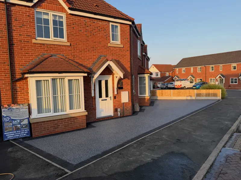 Light grey resin bound driveway with a charcoal block border in front of a modern red brick house on a residential estate.