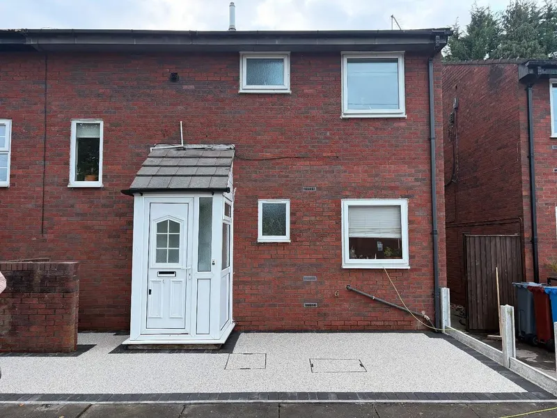 Wide light grey resin bound driveway bordered by dark block paving, including block frames around two rectangular covers in front of a red brick house.