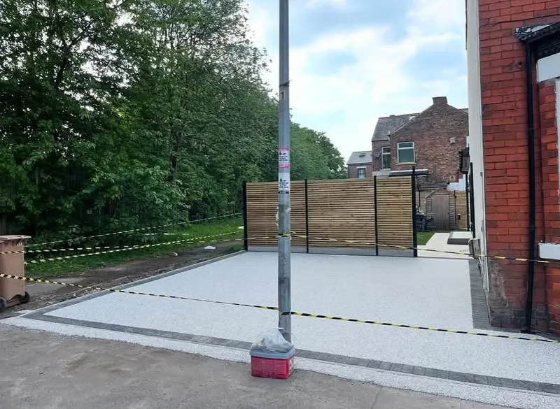 Newly laid light grey resin bound driveway edged with charcoal blocks in front of a red brick wall and slatted timber fence, protected by caution tape.