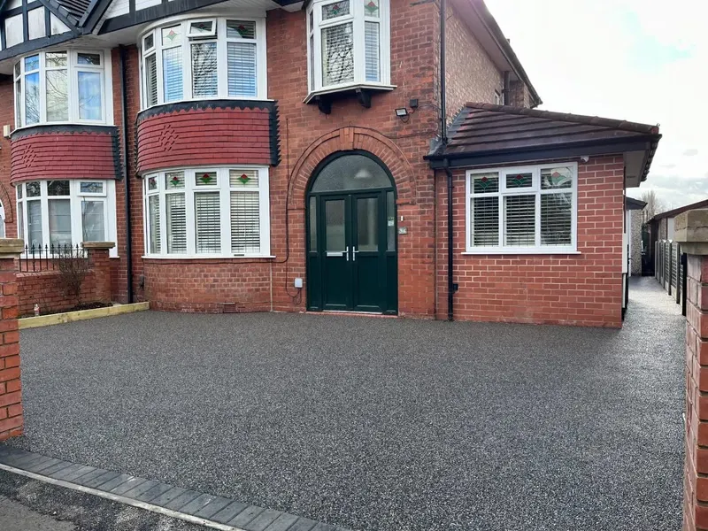 Dark grey resin bound surface covering the full front area and side passage of a red brick house, with a block paving edge at the street.