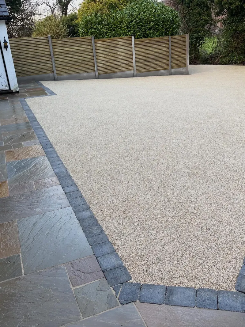 Large cream resin bound driveway section meeting a charcoal block border and adjacent multi-tonal natural stone patio slabs.