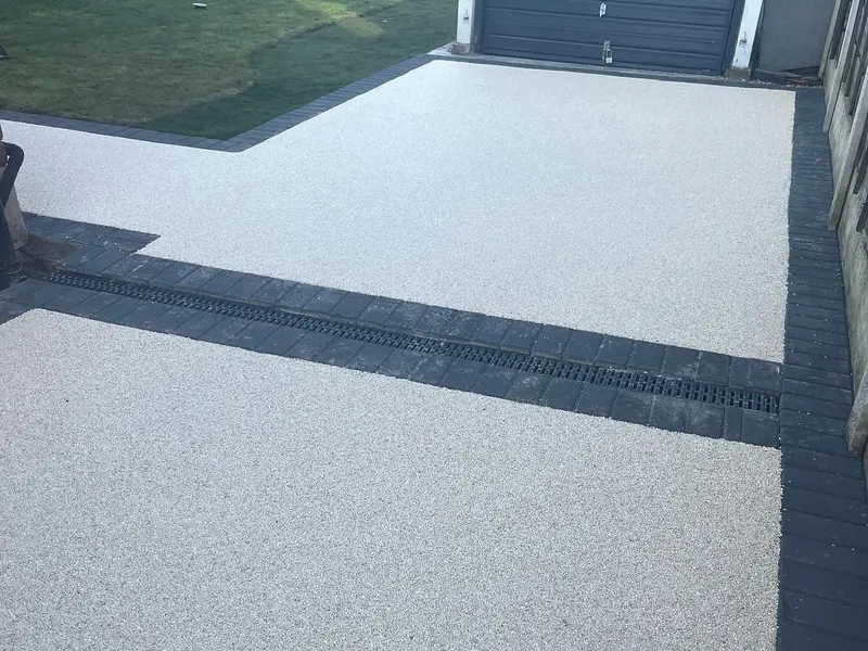 Off-white resin bound driveway and branching path bordered by charcoal blocks, with a black channel drain set into a double block course.