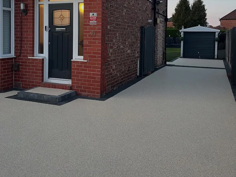 Light beige resin bound front drive and long side path with charcoal block edging, matching resin front step, and a grey side gate leading to a white garage.